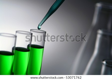 Laboratory pipette with drop of blue liquid over glass test tubes filled with green chemical solution for an experiment in a science research lab