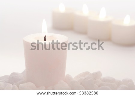 White votive candle burning softly with row of pastel color candles for meditation and purity celebration in high key faded mood fashion