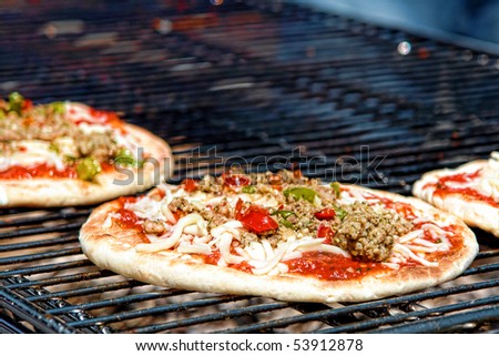 Pizza pie with sausage and peppers cooking on a charcoal grill in an Italian pizzeria