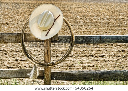 American West rodeo cowboy white straw hat and roping lasso hanging on an old wood fence post on an agriculture farm field at a Western ranch