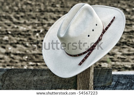 American West rodeo cowboy white straw hat on an old wood fence post on an agriculture farm field at a Western ranch
