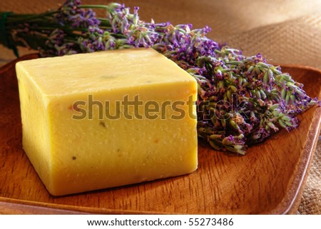 Block style bar of natural artisan aromatherapy soap with fresh lavender flowers in a wood dish
