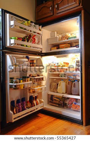 Top freezer kitchen refrigerator with doors open and shelves full of groceries with fresh and frozen food and cold bottles