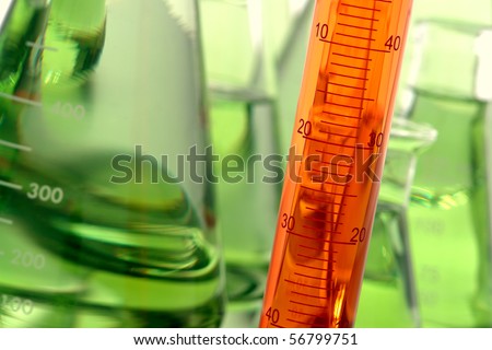 Graduated scientific cylinder filled with orange liquid and laboratory glassware full of green chemical solution for an experiment in a science research lab