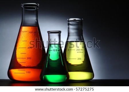 Laboratory glass conical Erlenmeyer flasks filled with red chemical with green and yellow liquid solution for an experiment in a science research lab