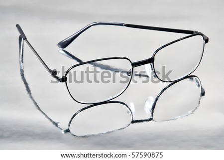 Pair of black polycarbonate contemporary reading glasses on shiny reflective metallic surface