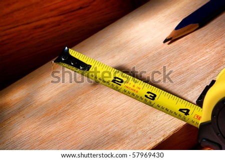 Self retracting construction tape measure and carpenter pencil on wood plank for a custom cabinetry woodworking project in a carpentry workshop