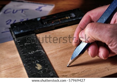Wood worker hand holding a carpenter pencil over a board with builder square tool during a construction project in a carpentry workshop