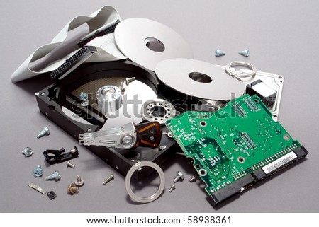 Crashed and broken apart dismantled computer hard drive with scattered component parts showing loose disks and circuit board with spread out assembly hardware