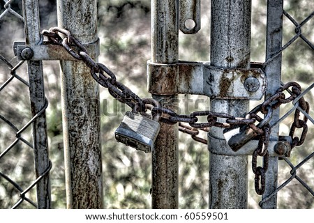Chain and locked padlock on a closed steel link fence gate at an abandoned industrial site