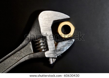 Adjustable spanner wrench jaw open around an industrial brass nut