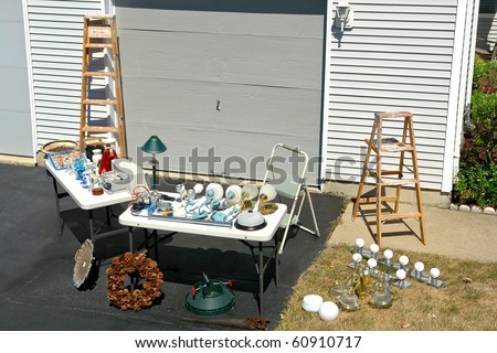 Garage sale with odd and ends objects for sale on tables at a suburban house yard driveway