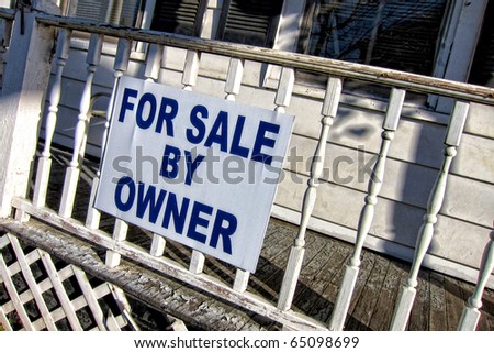 For sale by owner real estate sign hanging on the front porch railing of a poorly maintained old house