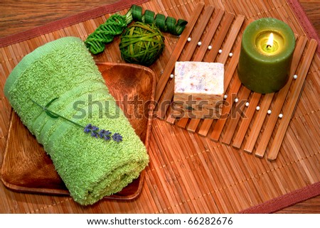 Soft green cotton towel in a wood tray with natural aromatherapy soap bar and candle burning for a pampering relaxation treatment in a spa