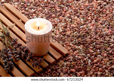 Meditation votive candle burning with a soft glowing flame on a wood mat over a bed of pea gravel in a religious temple