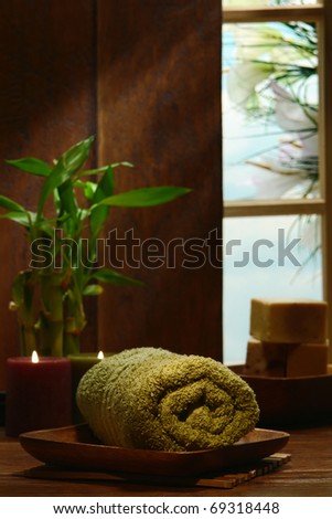 Soft green cotton towel rolled up in wood bathroom with candles burning and bamboo plant for a pampering relaxation treatment in a spa