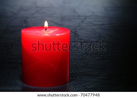Marbleized red pillar candle burning with a soft glow flame on a black leather surface