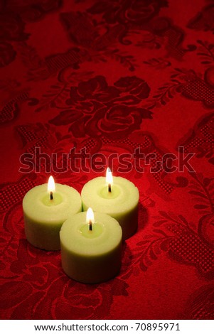 Green decorative wax candles burning with a soft glowing flame on a red damask fabric background