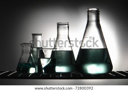 Chemical laboratory glassware with glass conical Erlenmeyer flasks and a scientific beaker with green chemistry liquid on a wire shelf for an experiment in a science research lab