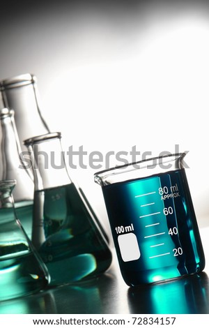 Glass scientific beaker filled with blue chemical liquid and laboratory conical Erlenmeyer flasks for a chemistry experiment in a science research lab