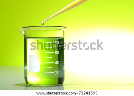 Pipette with drop of chemical above a glass scientific beaker with green liquid over bright yellow background for a laboratory chemistry experiment in a science research lab