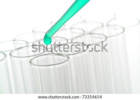 Pipette with green drop of chemical liquid solution above glass laboratory test tubes for a chemistry experiment in a biotechnology science research lab