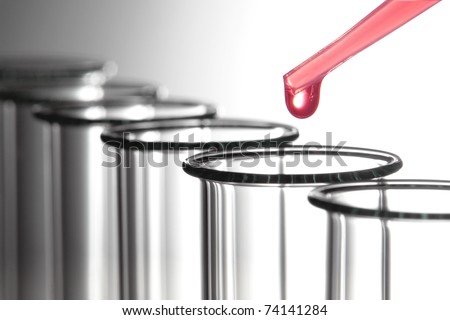 Laboratory pipette with drop of pink chemical liquid above empty test tubes for a biological chemistry experiment in an applied research science lab