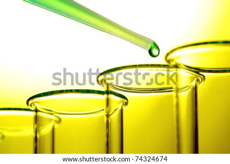 Laboratory pipette filled with green liquid and drop of chemical above empty test tubes backlit with yellow glow for a chemistry experiment in a science research lab