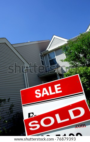 Real estate sold rider red insert on a Realtor advertising for sale sign in front of a house with blue sky