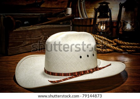 American west rodeo white straw cowboy hat on wood planks in a rustic ranch barn with old kerosene lamps burning and traditional western ranching tools