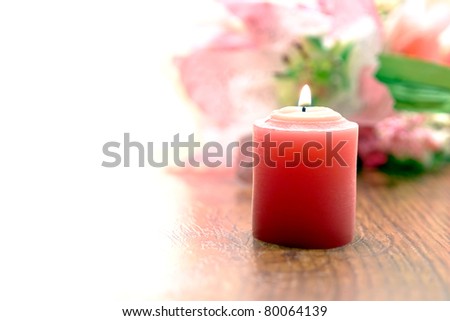 Pink votive candle burning with a soft glow before a pastel color flower bouquet in background over white