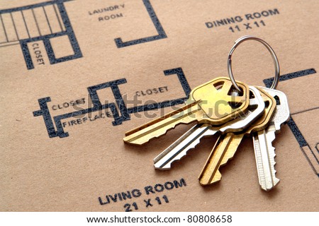 Set of house keys on a key ring over real estate home construction builder architectural floor plan printed on brown recycled paper