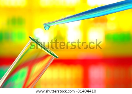 Laboratory pipette with drop of blue liquid chemical solution over glass test tube for an experiment in a science research lab