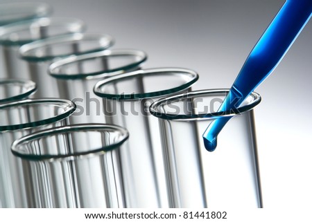 Laboratory pipette filled with cobalt blue chemical solution and emerging drop of liquid over row of empty glass test tubes for an experiment in a science research lab