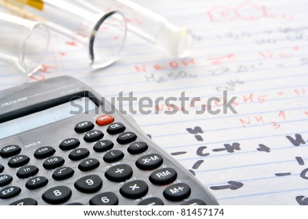 Scientific calculator with functions and  laboratory glass cylinders with test tube over notepad with hand written chemical formulas and applied results during an experiment in a science research lab