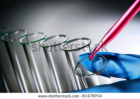 Laboratory pipette with drop of pink chemical liquid over glass test tube held in scientist hand for an experiment in a science research lab