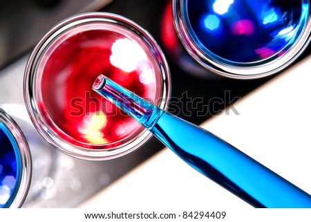 Laboratory pipette filled with blue liquid over glass test tube with red solution on a rack viewed from above for an experiment in a science research lab