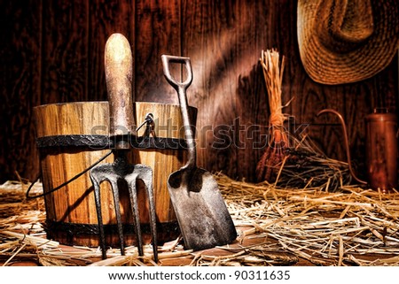 Antique gardening tools old steel shovel and vintage spading fork resting on an aged wood bucket in an older country garden shed