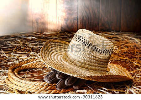 Old West farmer straw hat and gloves on a sisal ranching rope on hay covered wood floor in a dusty antique ranch hay barn hit by diffused sunlight