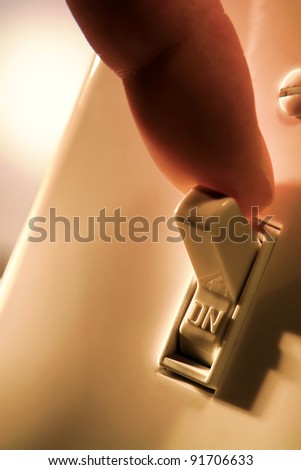 Electrician or homeowner finger turning off a traditional house wall North American electric light switch in the on position to turn home electrical lights out and conserve electricity energy