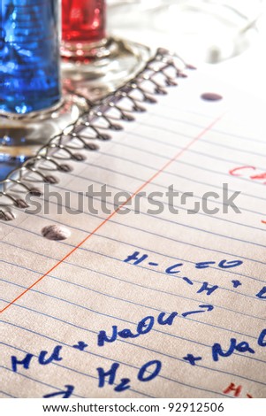 Hand written scientist chemistry formulas on a notebook page and laboratory scientific cylinder filled with red and blue liquids for an experiment in a science research lab