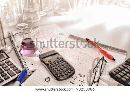 Pocket electronic scientific calculator and laboratory Erlenmeyer flask on notepads with hand written chemistry assay formulas and scientist notes for a chemistry experiment in a science research lab