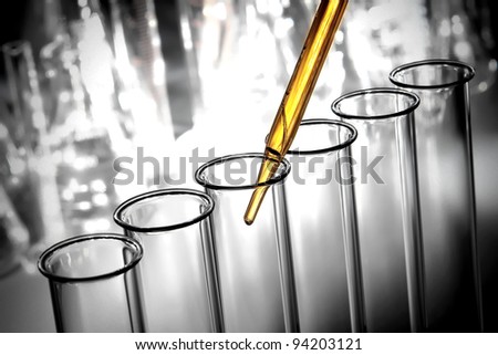 Laboratory pipette with emerging drop of yellow liquid over glass test tubes filled with chemical solution for a scientific experiment in a science research lab
