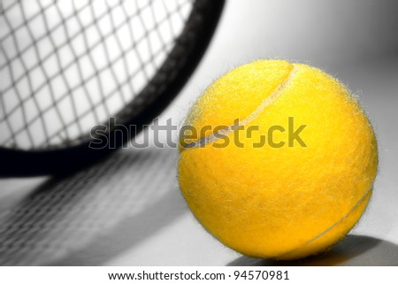 Bright yellow felt regulation championship tennis ball and sport racket on smooth court surface