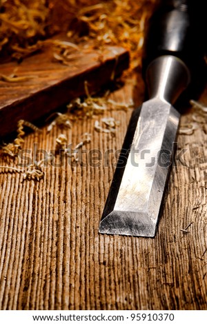 Used and worn carpenter wood chisel tool with loose shavings on old weathered distressed wooden board workbench in a vintage carpentry woodworking workshop
