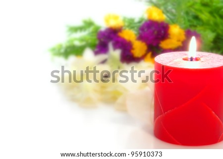 Red marble decorative pillar candle burning with a soft glowing flame in front of a blurry colorful flower bouquet on an elegant wedding reception festive white table