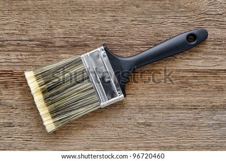 New nylon paint brush with black plastic handle and fine natural bristles on aged textured weathered wood boards workbench in a painter workshop