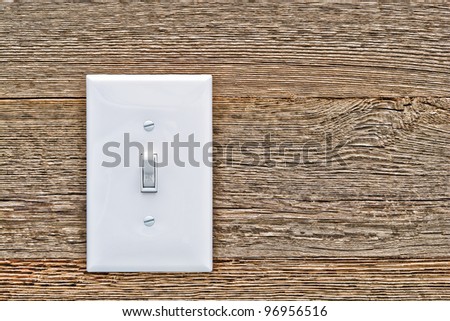 Traditional North American toggle white house electric light switch in ON position on aged old wood wall