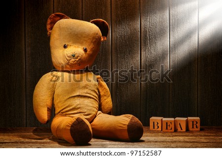 Old and used tan fabric vintage teddy bear stuffed animal toy with word spelled in antique alphabet blocks in an old house aged wood attic lit with filtered sunlight