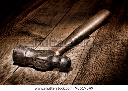 Antique wood handle forged steel ball peen blacksmith hammer on old aged and distressed wooden board workbench in a vintage maintenance and repair shop